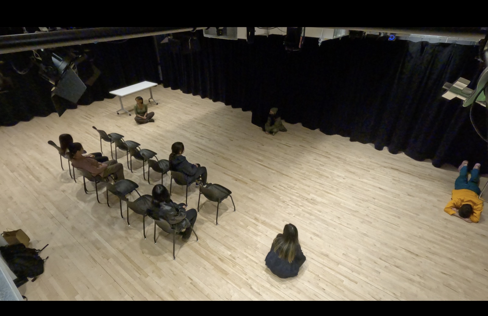 People sitting in two rows of chairs in a wooden-floored room.
